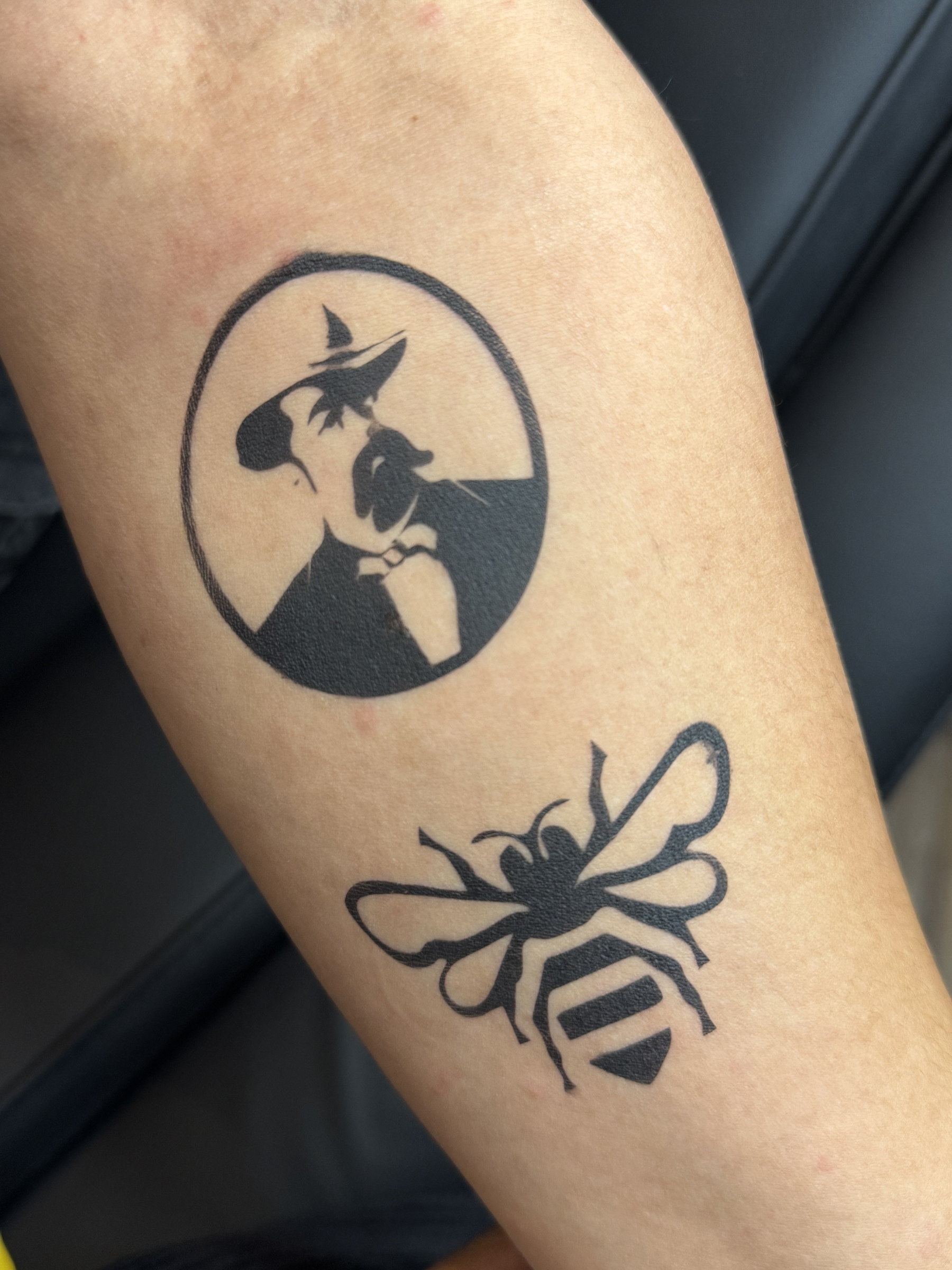 Airbrushed bee and hat tattoos on a forearm